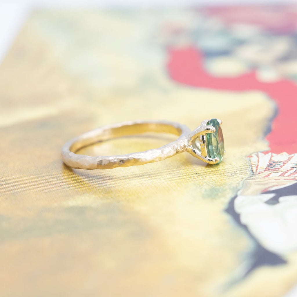 Side view on an abstract background of a handmade yellow gold solitaire ring with a beautiful green sapphire.