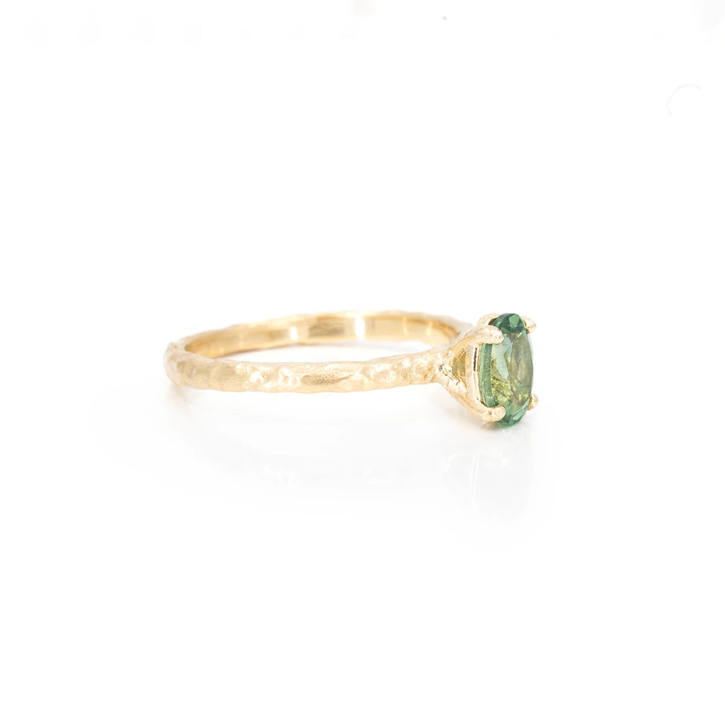 Side view on a white background of a hammered yellow gold ring featuring an oval green and yellow sapphire. This ring was handcrafted in Canada by independent brand Anouk Jewelry.