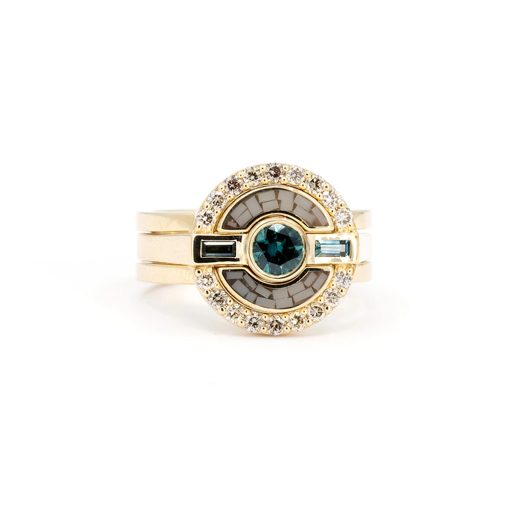 A massive ring with 3 gold bands shows a round face featuring a round teal sapphire in the center and two baguette teal sapphires on either side. These three sapphires are surrounded by a halo of round brilliant champagne diamonds and a unique composition made from lucite. These are actually two interlocking rings. One ring has a single band and the other a double band, giving the final look of three rings. This 2-in-1 engagement and wedding ring is a design by independent designer Erica Leal.