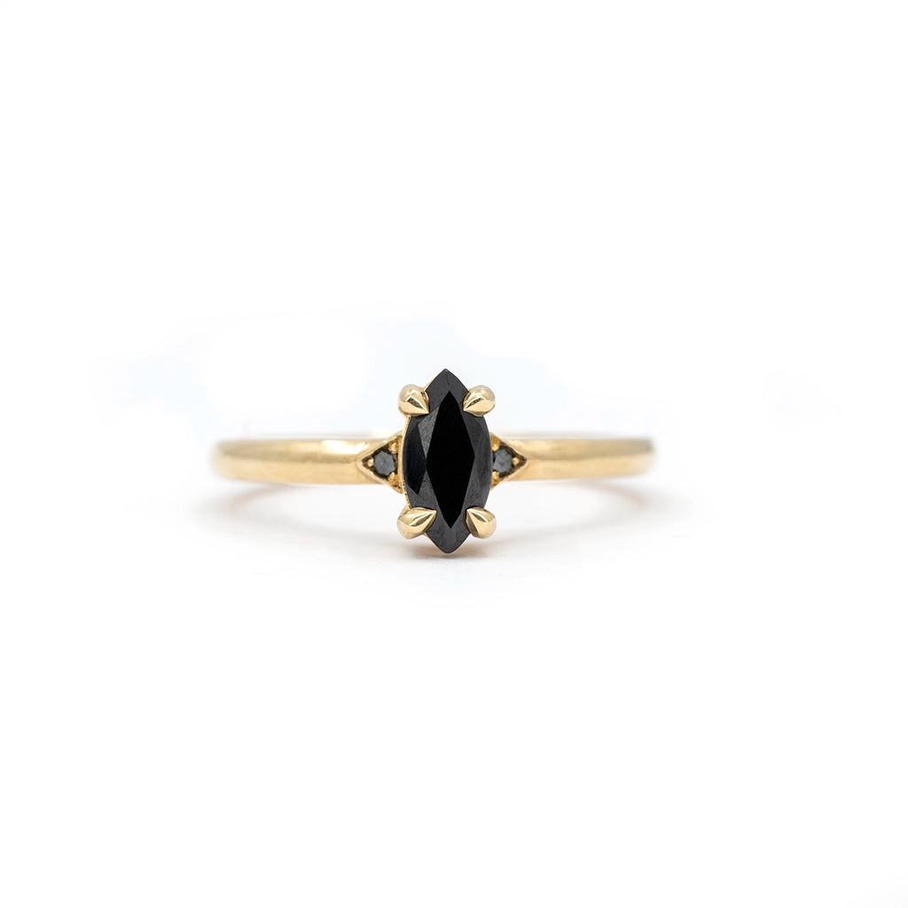 Front view of a marquise black gemstone set in yellow gold with hand-carved prongs and side black diamond details, designed by Canadian jeweller Liane Vaz.