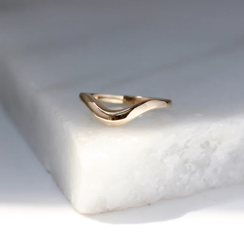 Polished 14k gold wave wedding band resting on a marble surface, handcrafted by Canadian designer Yuliya Chorna. Available at Ruby Mardi, fine jewelry Montreal.