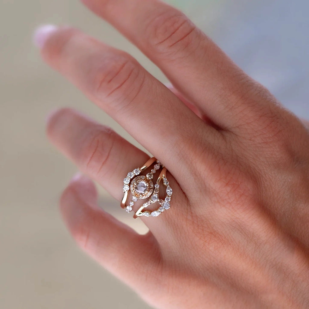 A hand wearing a sculptural bridal ring stack by Anastassia Sel, featuring a rose-cut diamond center ring framed by two curved diamond bands in yellow gold, available at Ruby Mardi in Montreal, Canada.