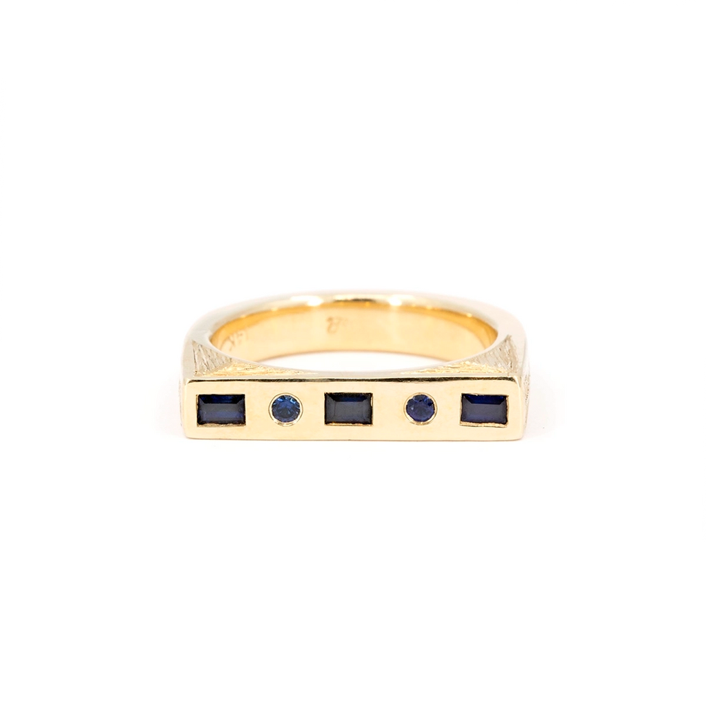 Yellow gold geometric ring by Rebel & Rogue Jewelry with alternating baguette and round blue sapphires and hand-engraved side details.