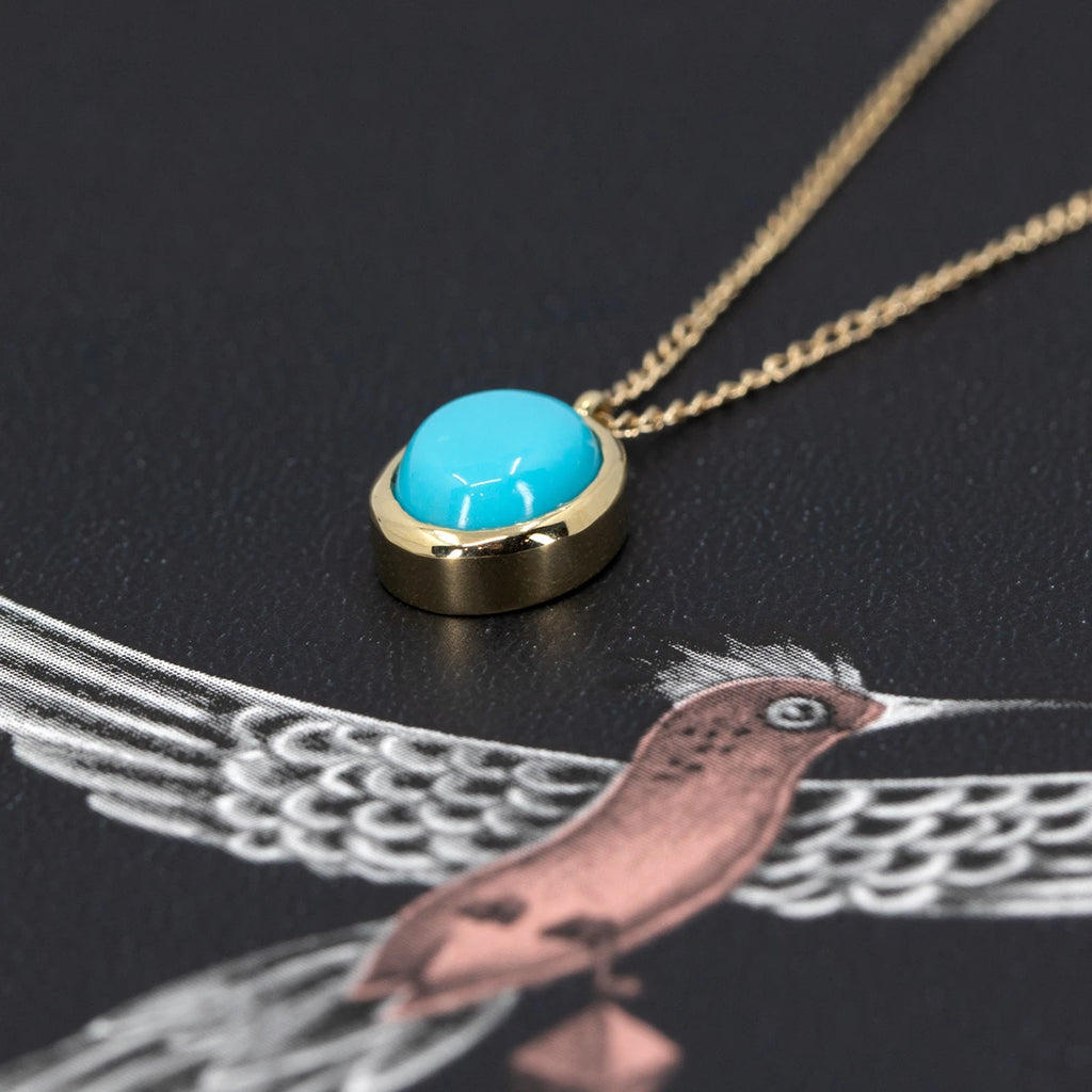 Close-up of a pendant with superb turquoise bezel set in solid gold. This designer pendant is seen photographed on a funky background from Emma J Shipley. This classic piece of jewelry is available at the Montreal jewelry store Ruby Mardi. 