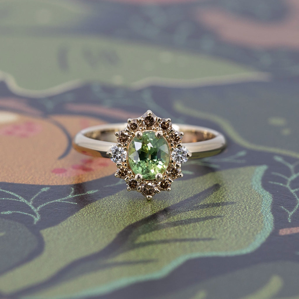 Unique green sapphire engagement ring with champagne and white diamond halo, set in yellow gold, photographed on a colorful background.