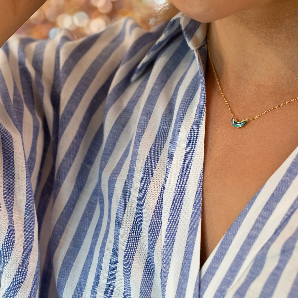 Artistic photo of Emily Gill’s curved gold pendant necklace with turquoise enamel and diamonds, sold at Ruby Mardi, Montreal fine jewelry boutique.