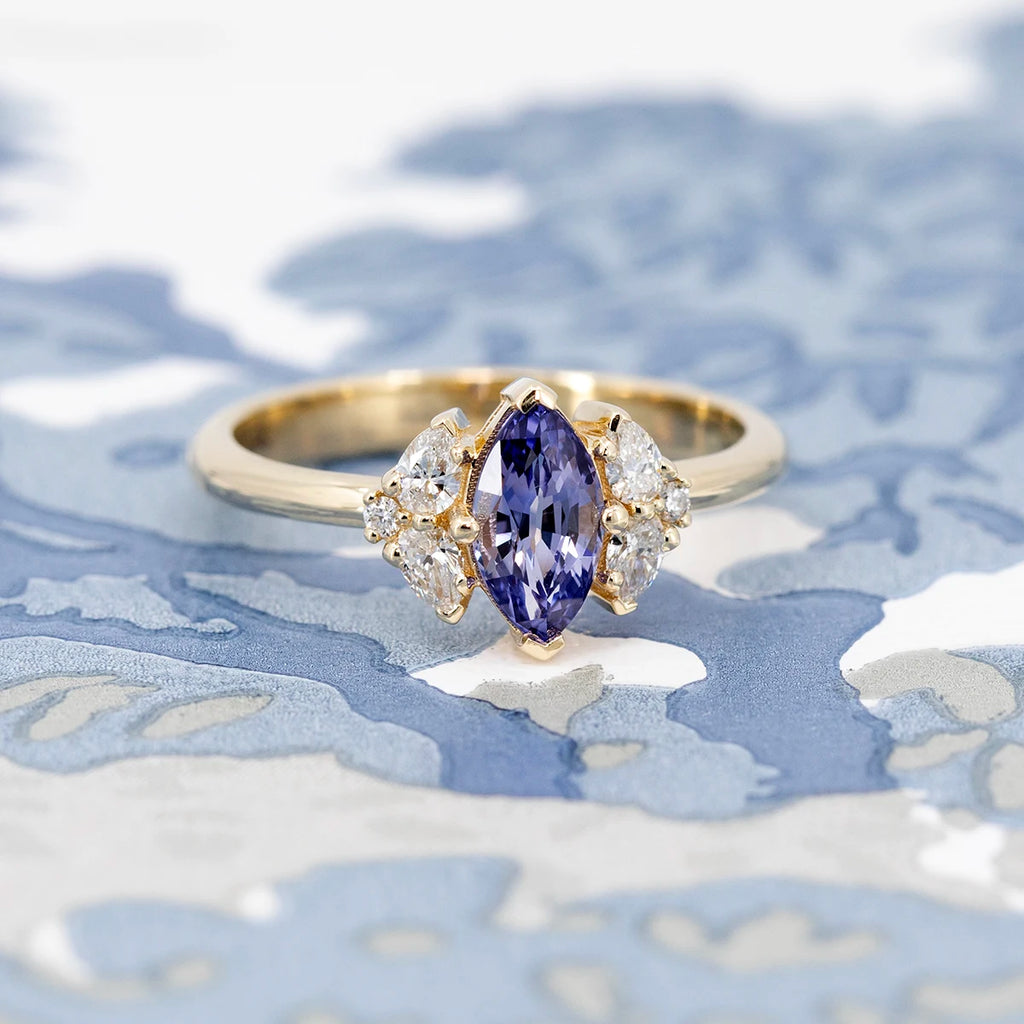 Artistic flatlay of a marquise purple sapphire engagement ring with diamonds, placed on a blue patterned background.