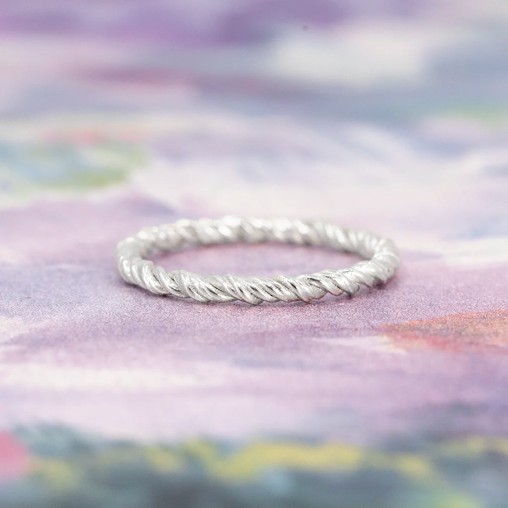 Twisted white gold ring with a textured finish, handmade in Montreal. Unique minimalist wedding band by Ruby Mardi, photographed on a soft pastel background.