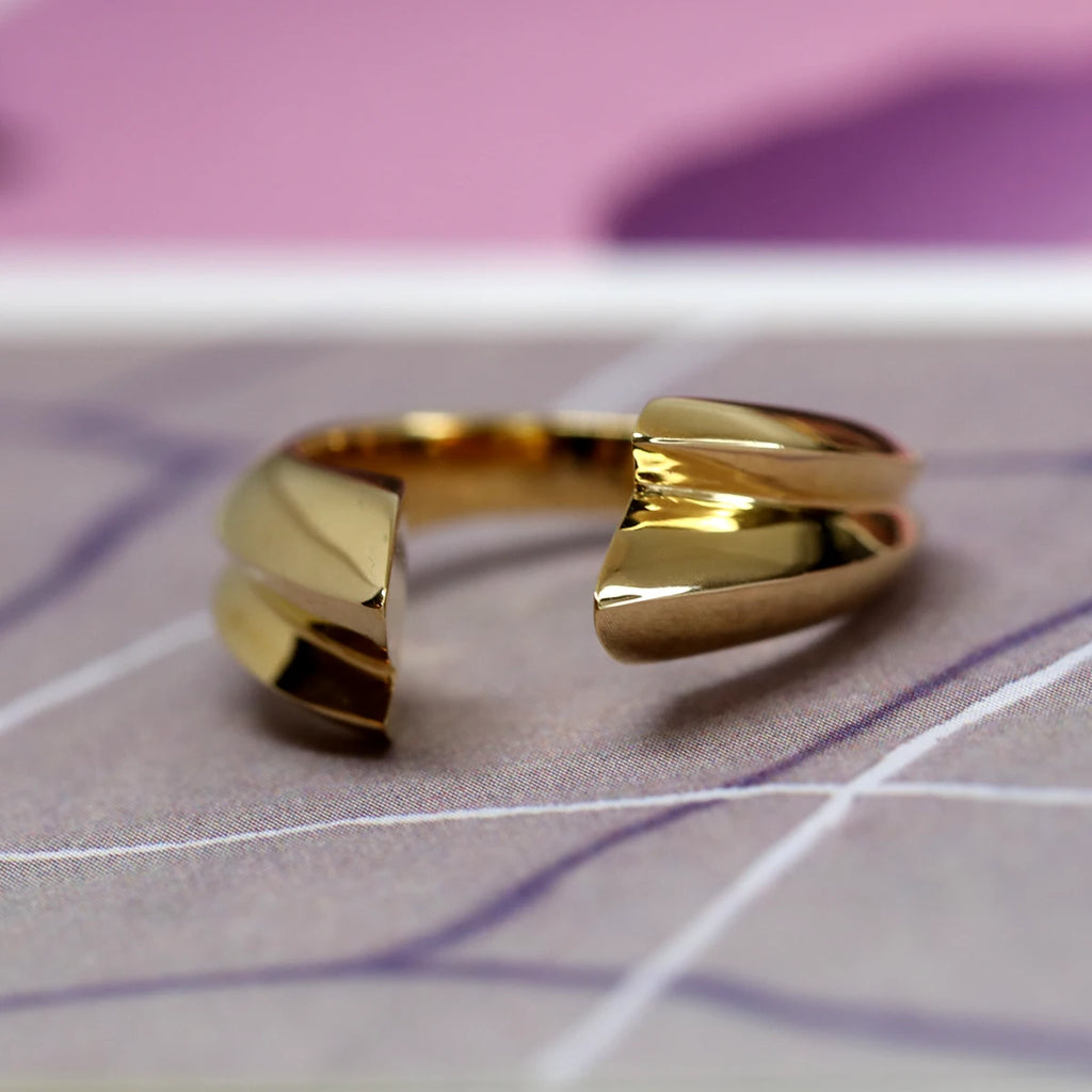 Open vermeil designer ring in close up photographed on a pinkish/mauve abstract background.