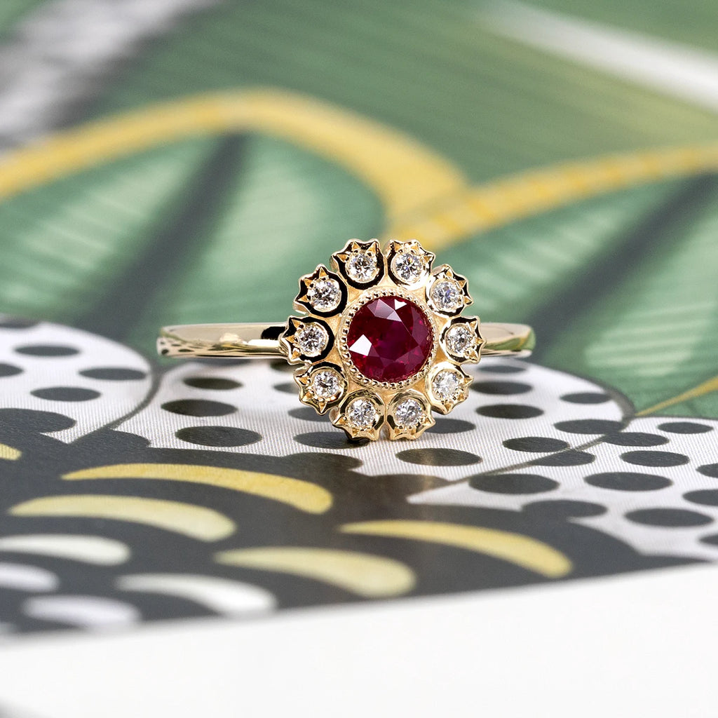 The one-of-a-kind engagement ring, made by Canadian designer Bramston Goldsmithing, is composed of a round ruby in a bezel setting, with a delicate miligrain to give it a revisited vintage style, is composed of a diamond halo with a flower or cat pattern. This handmade bridal ring is available for sale at the Ruby Mardi jewelry store and jewelry gallery located in the Villeray and Rosemont neighborhoods.
