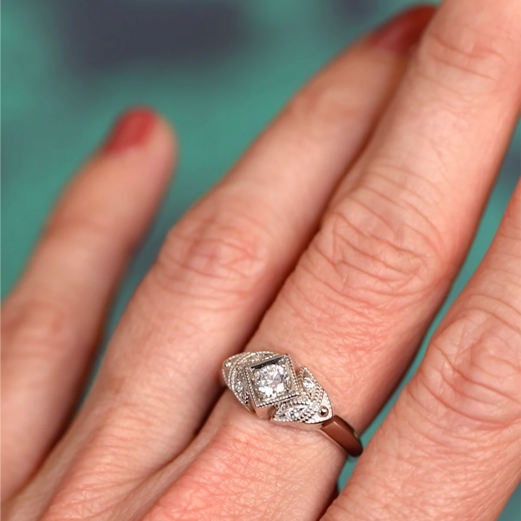 Art Deco white gold engagement ring with round diamond framed in a square setting, worn on hand. Milgrain and diamond details. By Deborah Lavery for Ruby Mardi, Montreal.