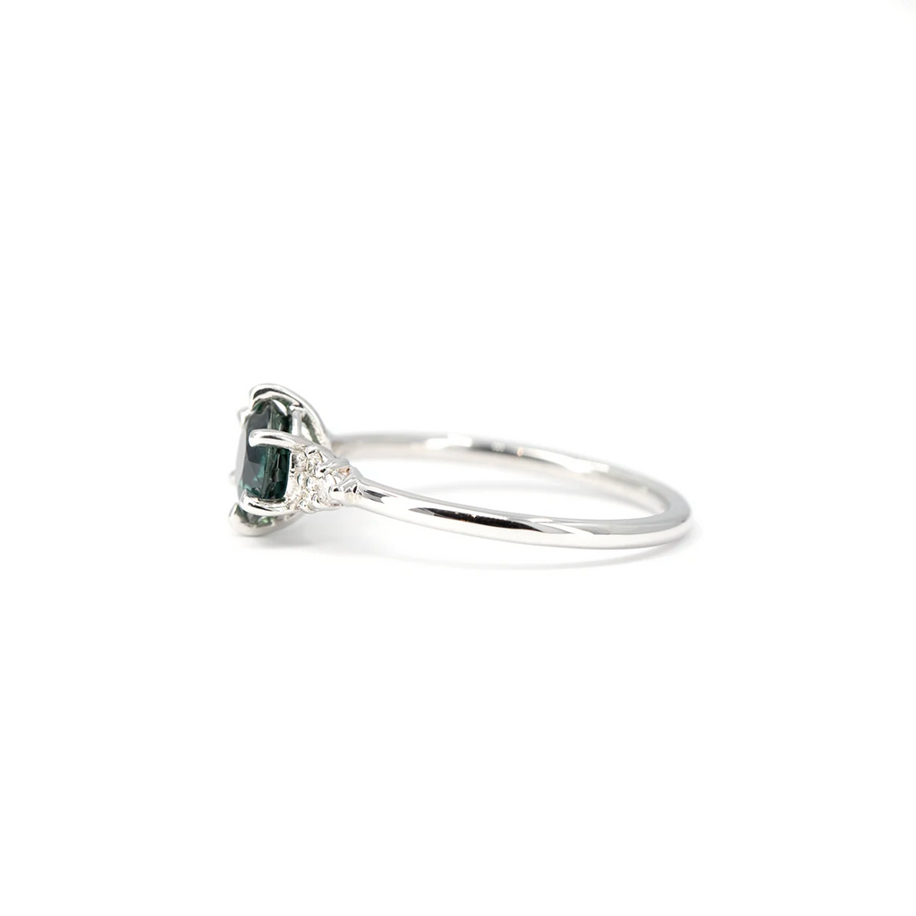 Side view showing the prong setting of a round teal sapphire and white diamond ring in 14k white gold. Handmade in Montreal by Maksym Jewelry, available at Ruby Mardi.