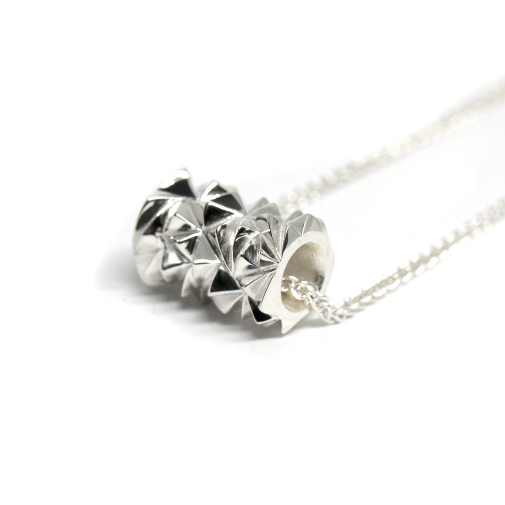 Close-up of a white gold faceted tube pendant by Bena Jewelry, featuring a geometric design that reflects light. Suspended on a delicate white gold chain, this modern statement piece blends bold style with elegance. Available at Ruby Mardi, a collective of independent designer jewelry in Montreal.