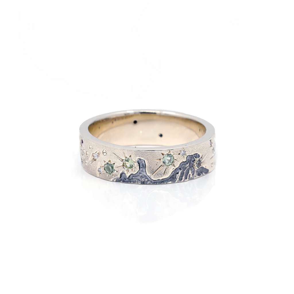 Splendid men's ring with handmade engraving representing a starry sky and set with several natural green gems. This gold ring is made in Canada by independent alternative bridal jewelry designer Janine de Dorigny. This unique piece of jewelry is available for sale at the Ruby Mardi jewelry gallery and jewelry store in Montreal.