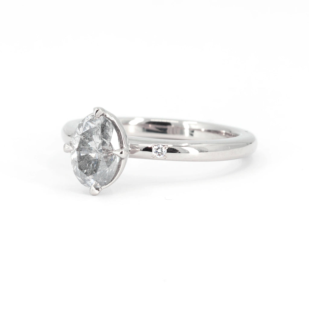 Side view of an oval grey salt & pepper diamond solitaire ring from Canadian designer Yuliya Chorna. Two small natural diamonds are inlaid in the 14k white gold ring. This one-of-a-kind jewelry piece is available at the best jewlery store in Canada, Ruby Mardi.
