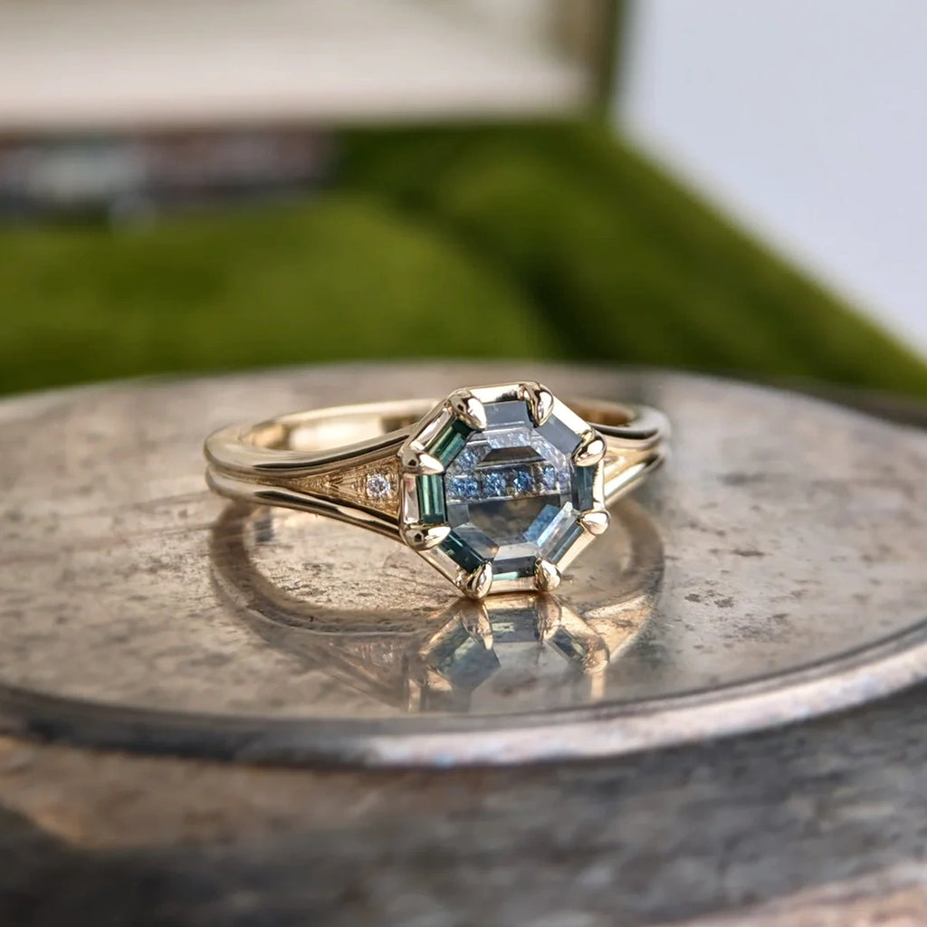 Octagon-cut Montana sapphire ring with diamond accents on a split shank 14k yellow gold band, designed by Emily Gill. Shown on vintage surface, photographed at Ruby Mardi in Montreal.