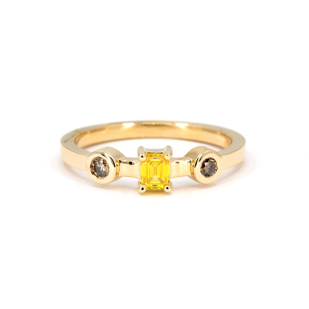 Yellow gold ring featuring an emerald-cut yellow diamond flanked by two round brown diamonds in bezel settings, modern alternative engagement ring available at Ruby Mardi.