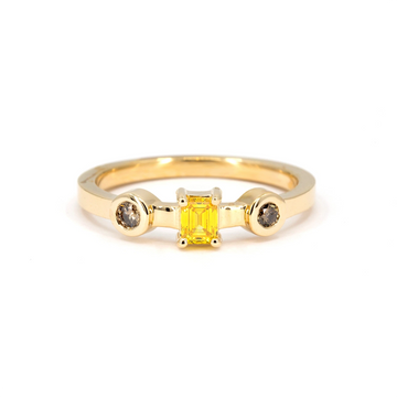 Yellow gold ring featuring an emerald-cut yellow diamond flanked by two round brown diamonds in bezel settings, modern alternative engagement ring available at Ruby Mardi.