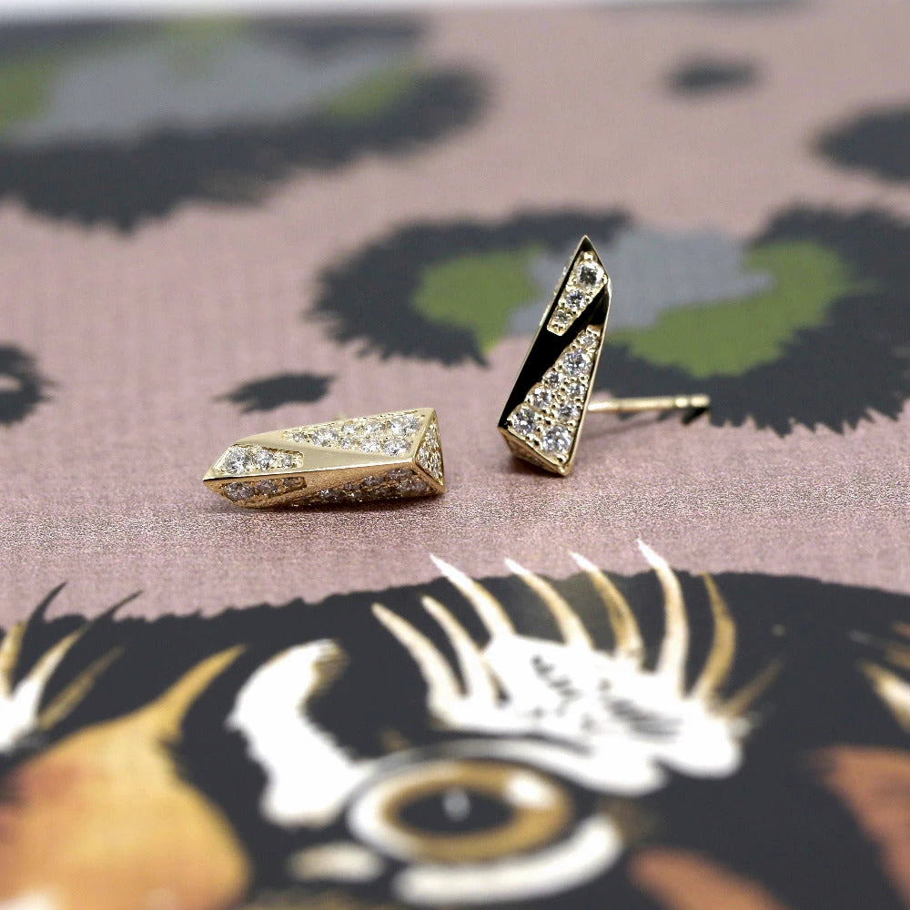 A photography of a fashion and modern pair of gold diamond stud earrings taken on a drawing of a tiger. These earrings show indeed a lot of power and energy. These unisex studs are an original design from designer Bena Jewelry.