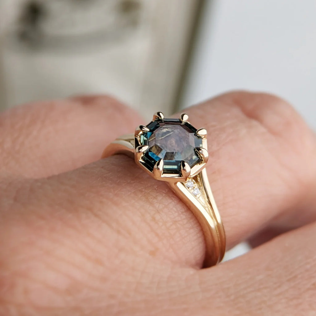 Montana sapphire ring in yellow gold with diamond accents, worn on hand. Octagonal portrait-cut center stone with split shank, designed by Emily Gill for Ruby Mardi, Montreal.