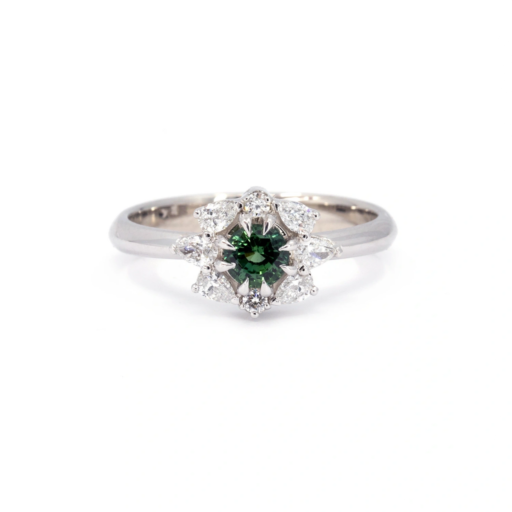 Elegant Alpine Star ring featuring a vibrant green sapphire at its center, surrounded by a dazzling diamond halo in a floral-inspired white gold setting. A unique alternative engagement ring, handcrafted by Ruby Mardi in Montreal.