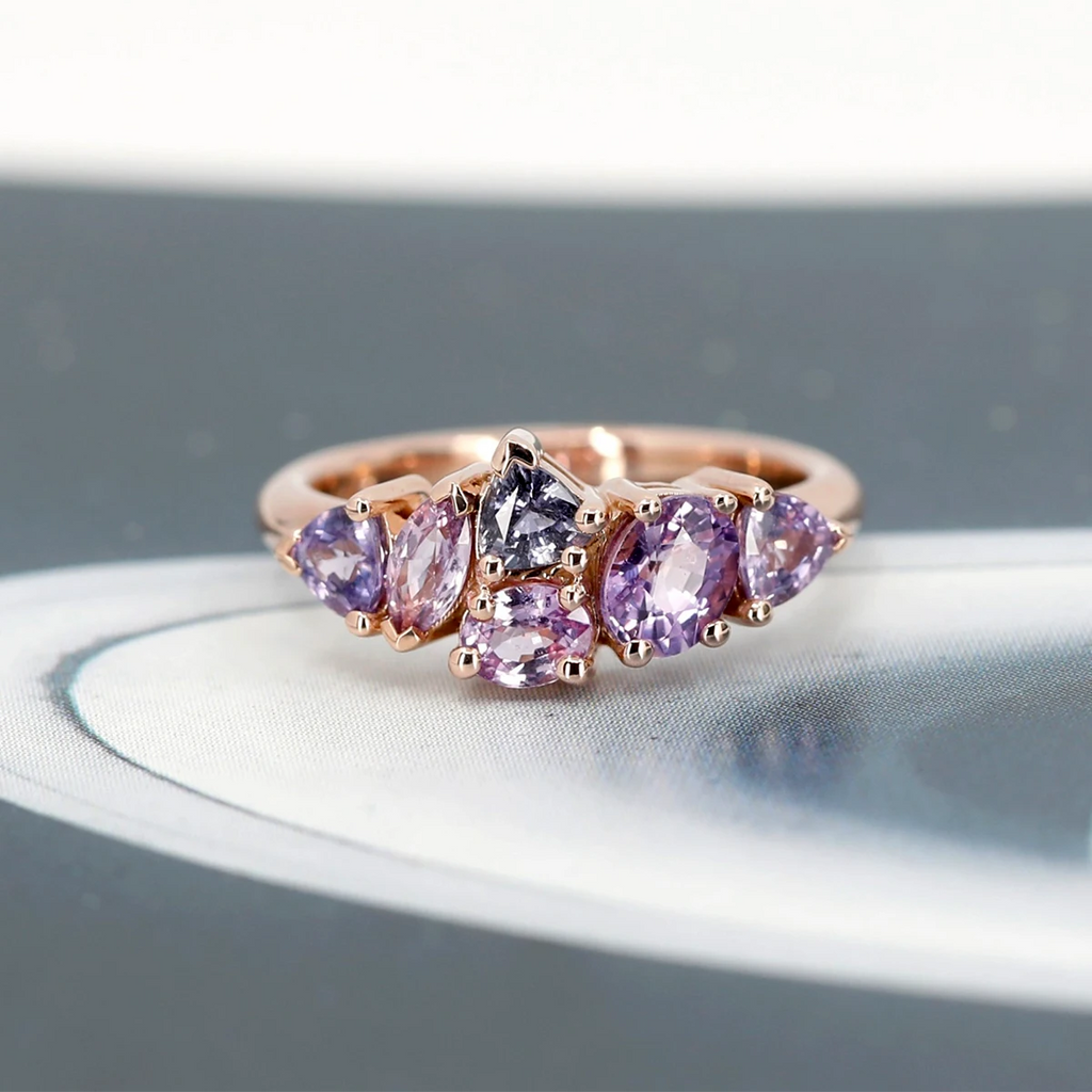 Rose Gold ring and 6 natural sapphire gems in hues of lilac, mauve and purple. The beautiful one-of-a-kind ring is photographed on a funky abstract background.