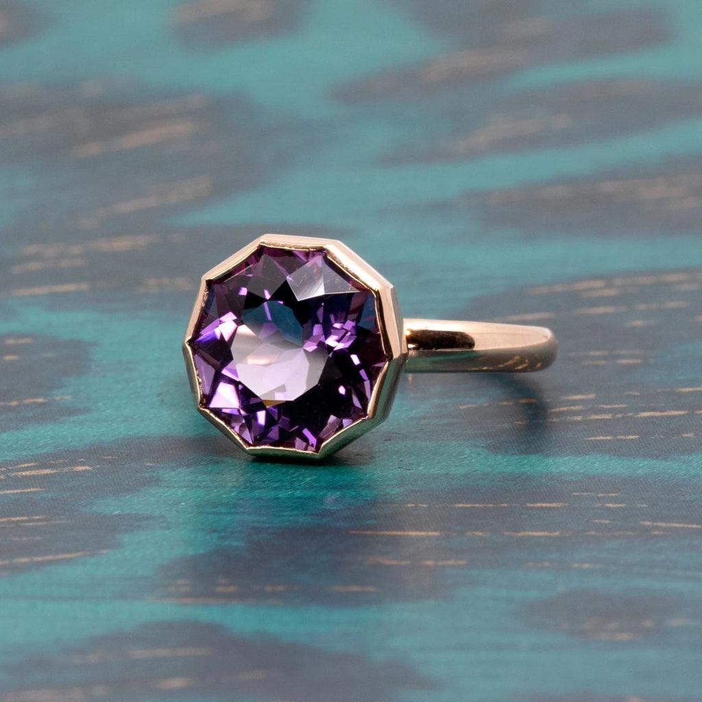 A big cocktail ring photographed in side view, making the the light enter in the big amethyst it features. This gender neutral statement ring is set in rose gold and was designed and handcrafted in Montreal.