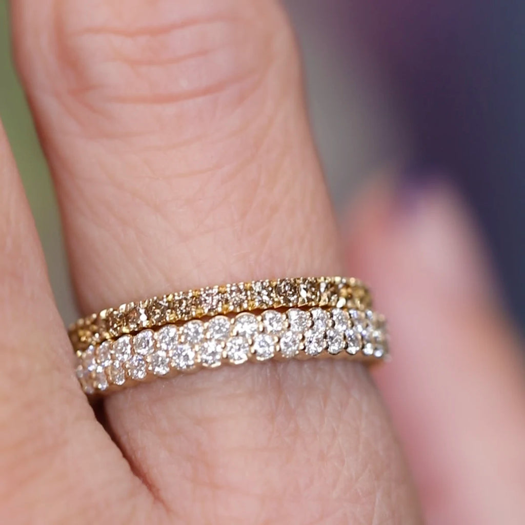 Close-up of a yellow gold full eternity band set with warm brown diamonds, worn on a finger. The ring sits above a white diamond eternity band, showcasing the contrast between the two designs. Photo taken at Ruby Mardi Jewelry in Montreal.