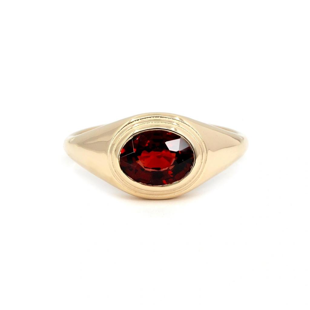Yellow gold ring featuring an oval-cut deep red pyrope garnet in a bezel setting. Handmade in Montreal by Bena Jewelry, this bold unisex design combines modern minimalism with vintage signet ring inspiration. Shown on a white background.