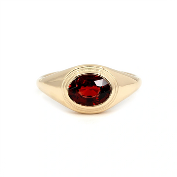 Yellow gold ring featuring an oval-cut deep red pyrope garnet in a bezel setting. Handmade in Montreal by Bena Jewelry, this bold unisex design combines modern minimalism with vintage signet ring inspiration. Shown on a white background.