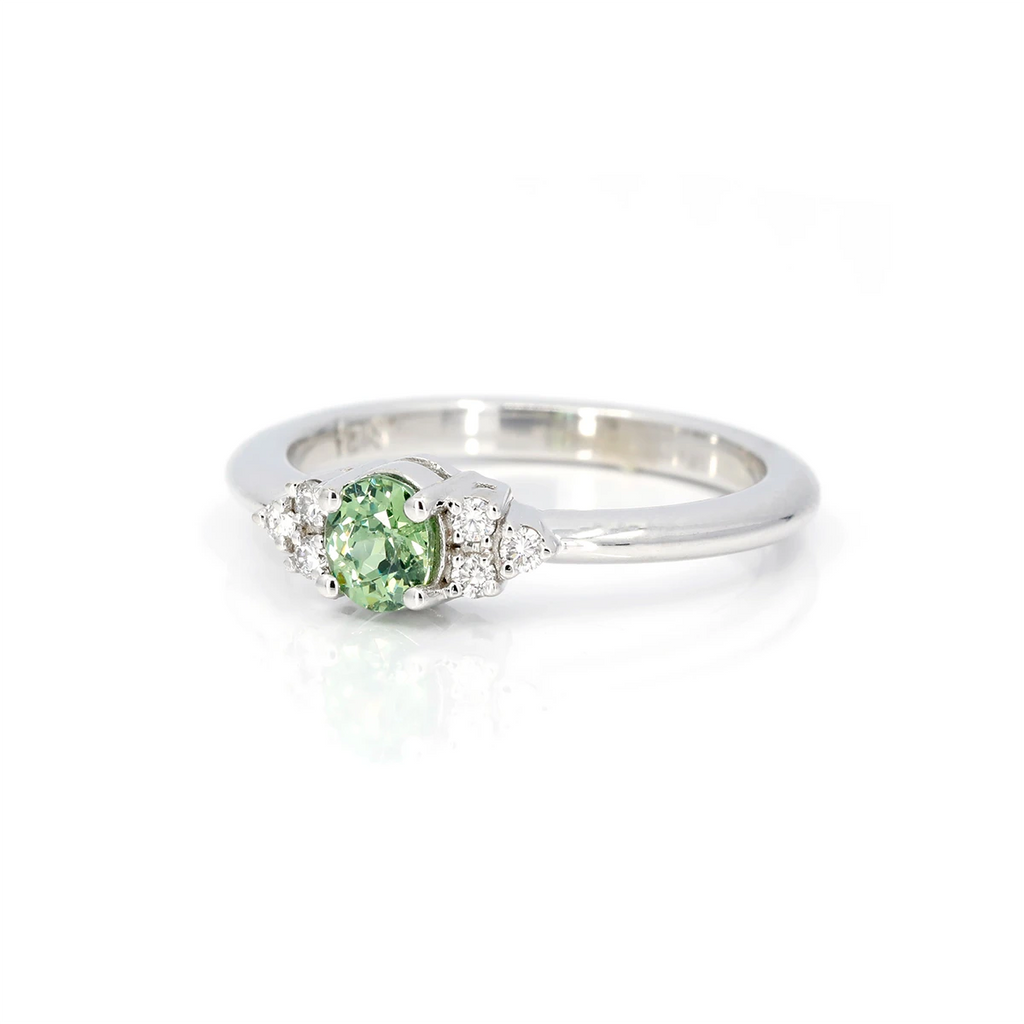 Side view in close up of a white gold bridal ring with a central green garnet gem and 6 small round natural diamond accents. 
