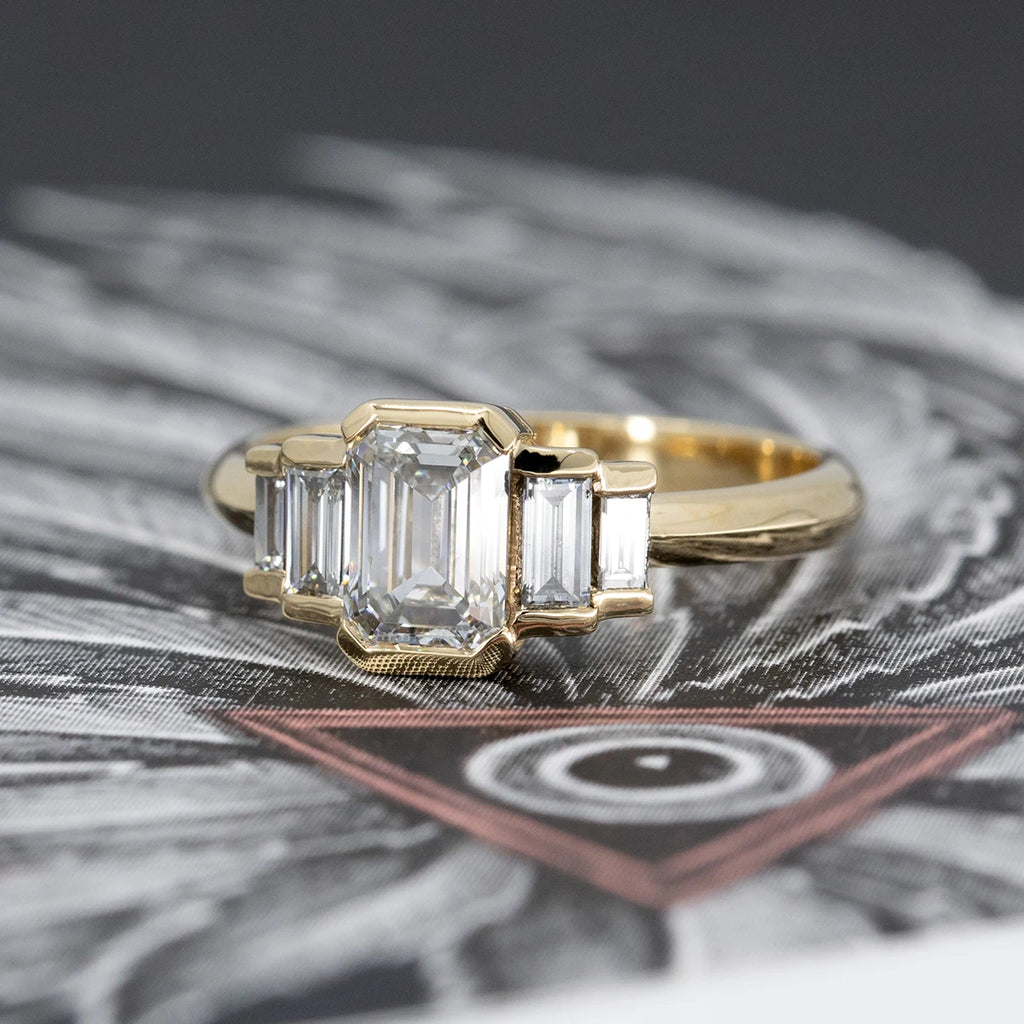 Emerald-cut diamond engagement ring with stepped baguette diamond sides in bezel setting, crafted in yellow gold. Bold Art Deco style ring from Ruby Mardi, fine jewelry store in Montreal, Canada.