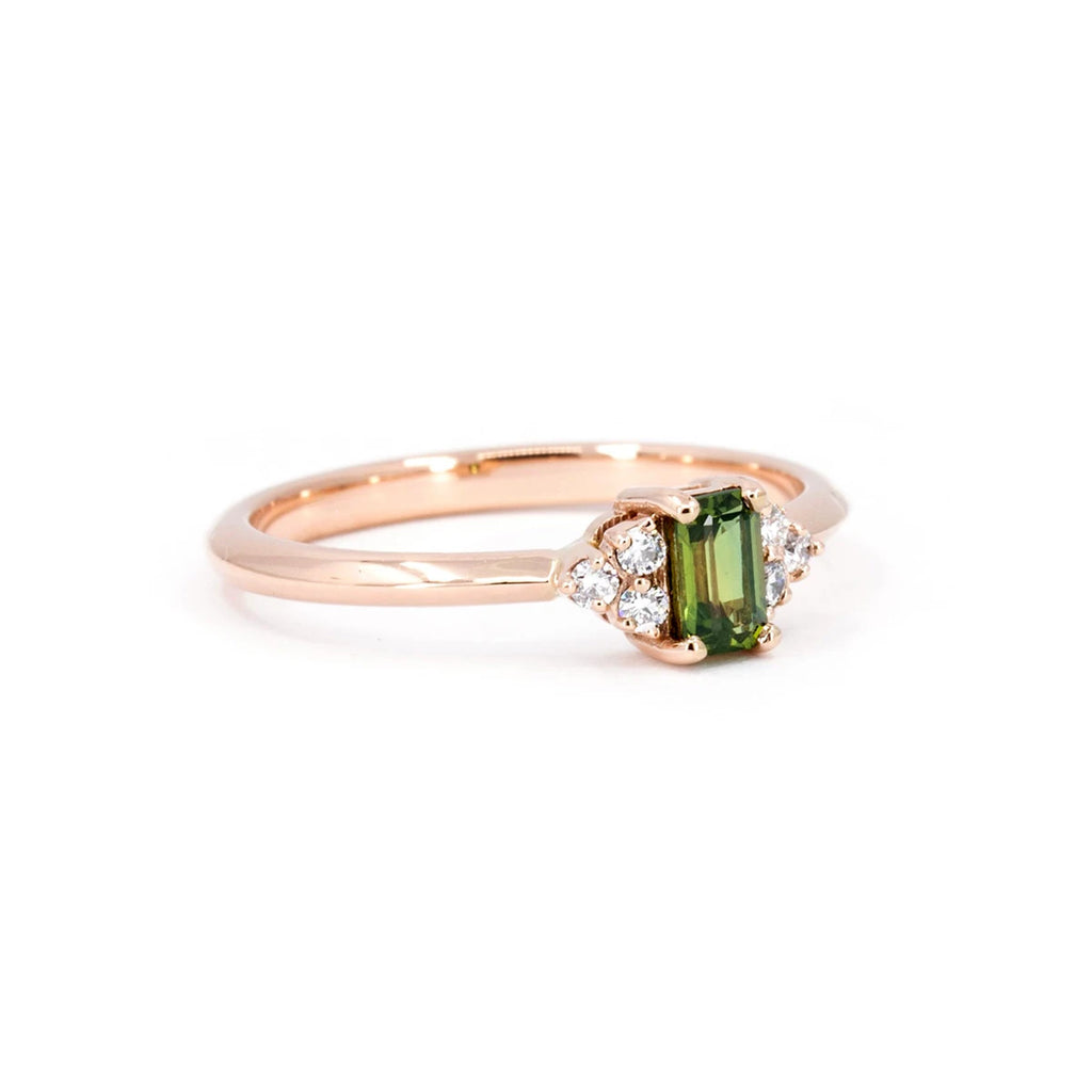 Side view of a delicate engagement ring with a central emerald shape green sapphire and three round diamonds on each side. Classic piece of jewelry handmade in Montreal by Ruby Mardi, the best jewelry store in Canada.