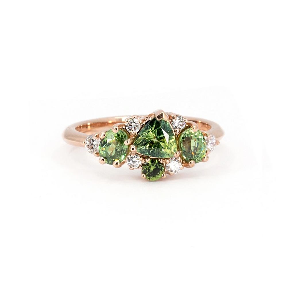 Rose gold ring by Ruby Mardi featuring a cluster of lab-grown diamonds, green sapphires, and demantoid garnets. Photographed on a white background, this unique design showcases vibrant gemstones in a harmonious arrangement.