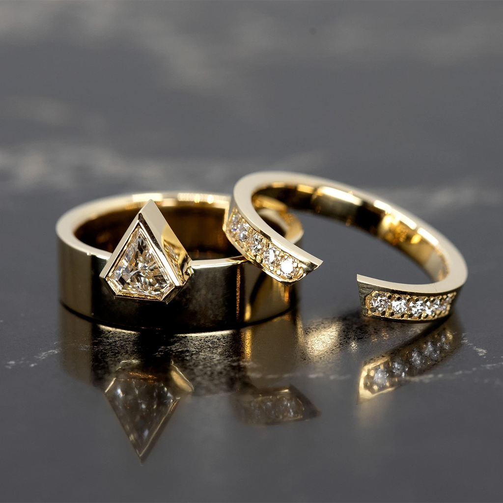 A gold open ring with 10 small diamonds is seen photographed with its matching ring: a chunky gold band mounted with a pentagonal lab grown diamond. This designer and modern set of fashion jewellery was designed in Montreal by Bena Jewelry and is seen here photographed on black marble.
