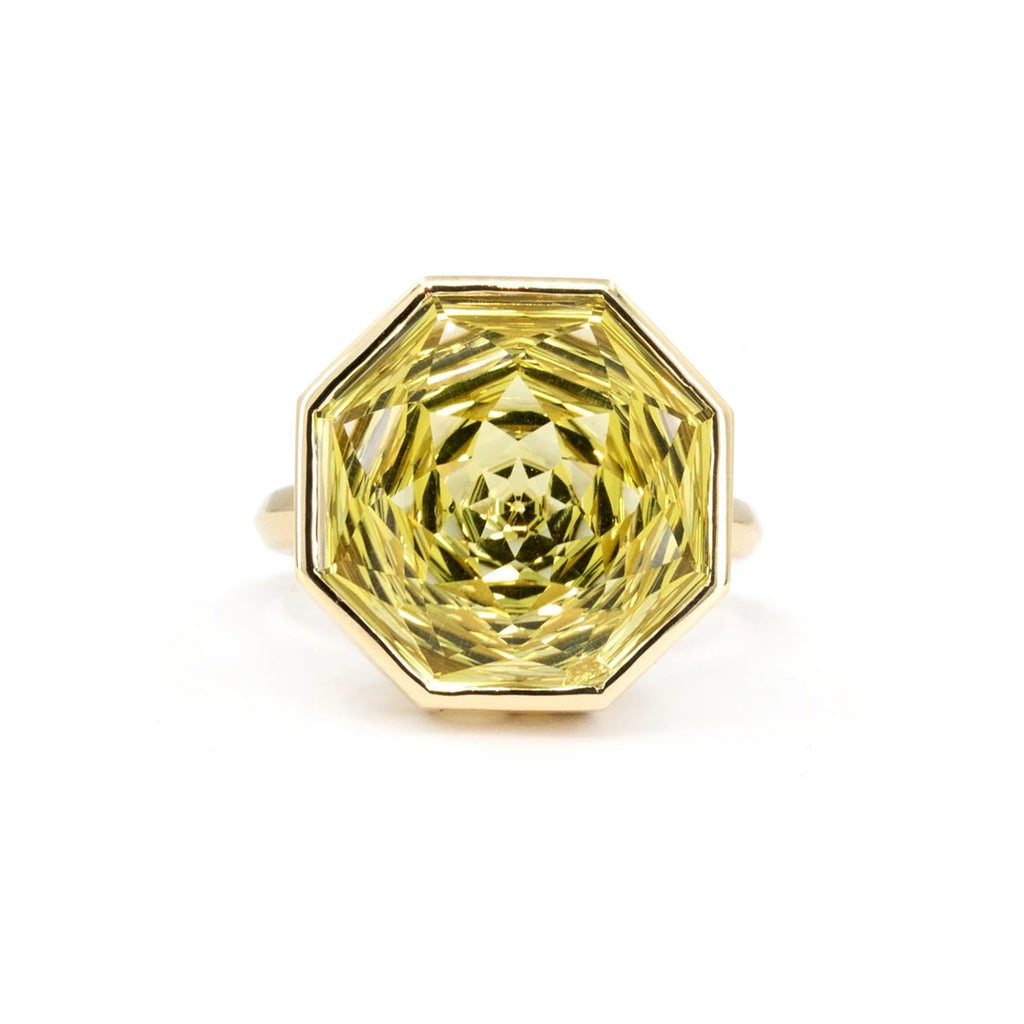 A large ring seen from the front, photographed against a white background. The gem is octagonal in shape, with a yellow-green color. The gemstone is so large that the ring band is barely visible behind it. It is set in 14-carat yellow gold. This is a unique creation by Canadian jewelry designer Bena Jewelry. 