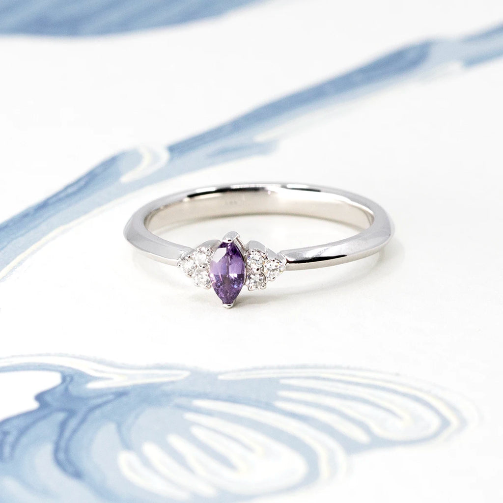 Dainty engagement ring photographed on a flowery background. The bridal ring features a marquise purple sapphire and natural diamond accents on each sides. Handmade and designed in Canada by Ruby Mardi, the best Canadian jewelry store.