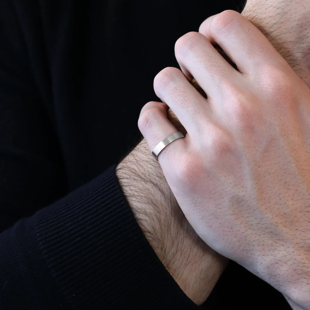 Close up on a man wearing a black sweater and a satin matte white gold wedding ring. This classic band was handmade in Montreal by independent brand and jewelry store Ruby Mardi.