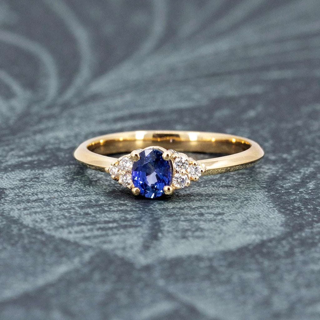 A dainty and classic feminine engagement ring featuring a royal blue sapphire and natural diamond accents is seen photographed on a vegetal background. This bridal ring is a design from Ruby Mardi, an independent Canadian jewelry store that also sell the work of many talented jewellery designers.