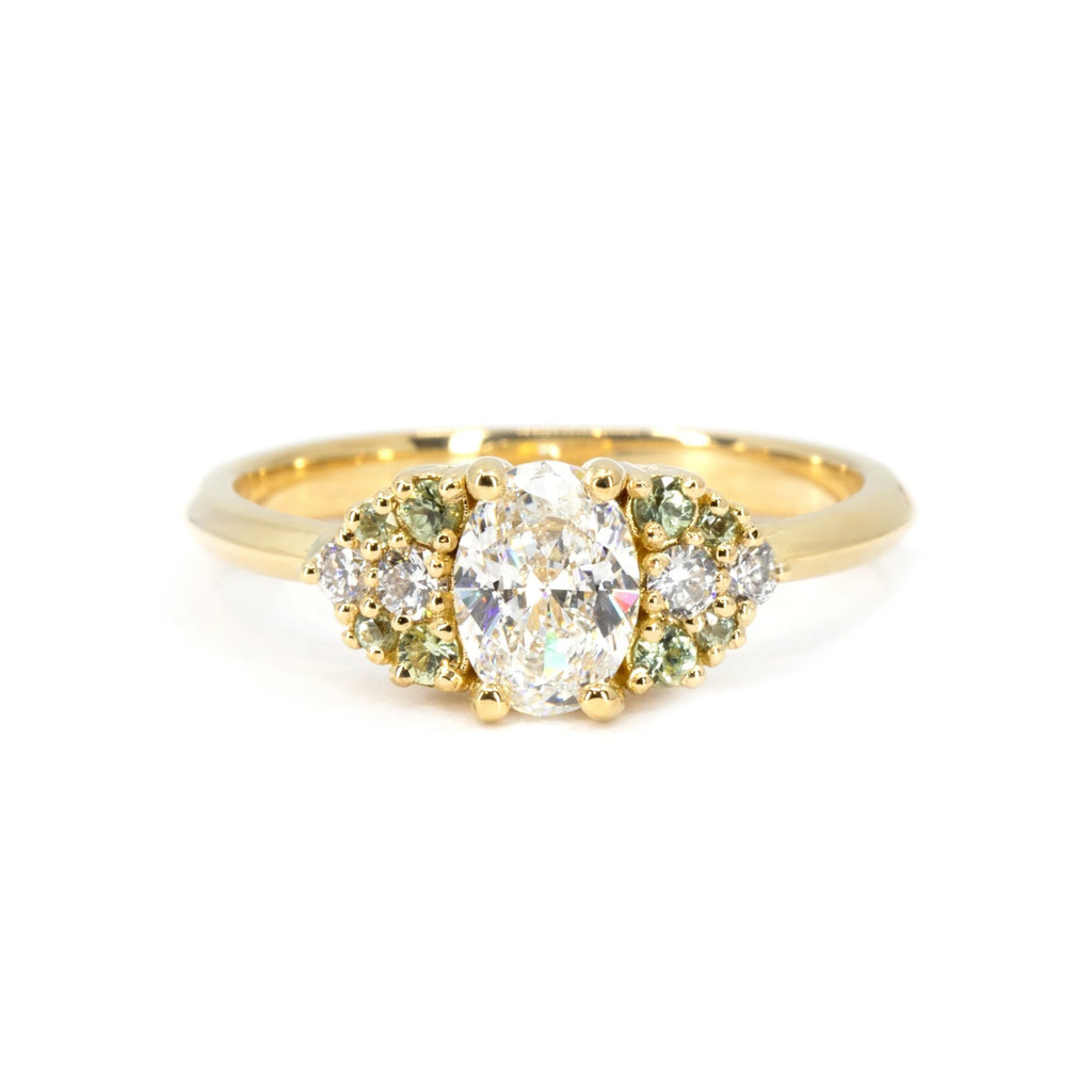 Yellow gold engagement ring featuring an oval diamond center, framed by green sapphires and white diamonds. Designed by Bena Jewelry, made in Montreal.








