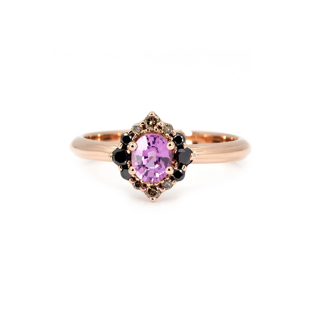 Ruby Mardi signature engagement ring in rose gold, featuring an oval pink sapphire at the center, surrounded by a unique cluster of black diamonds, champagne diamonds, and grey diamonds. Bold yet romantic design handcrafted in Montreal by Ruby Mardi, an independent Canadian jewelry house known for expressive and unconventional bridal pieces.