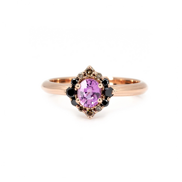 Ruby Mardi signature engagement ring in rose gold, featuring an oval pink sapphire at the center, surrounded by a unique cluster of black diamonds, champagne diamonds, and grey diamonds. Bold yet romantic design handcrafted in Montreal by Ruby Mardi, an independent Canadian jewelry house known for expressive and unconventional bridal pieces.