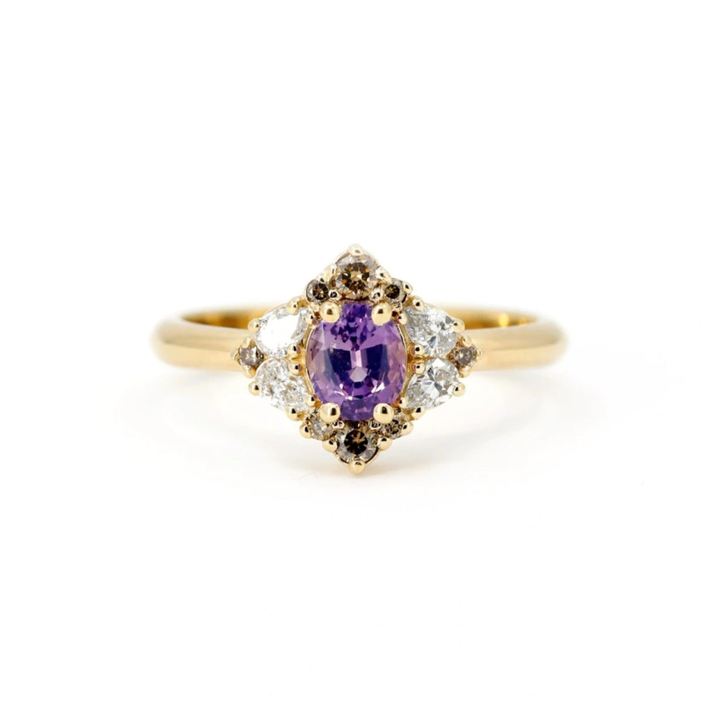 Alternative engagement ring handmade in Montreal by Ruby Mardi, featuring an oval purple sapphire center stone set in warm yellow gold. Surrounded by a vintage-inspired halo of natural brown diamonds and sparkling white accent diamonds, this unique designer ring blends bold color with refined symmetry. A one-of-a-kind fine jewelry piece that showcases Ruby Mardi’s artistic approach to gemstone design and unconventional bridal styles.