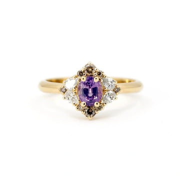 Alternative engagement ring handmade in Montreal by Ruby Mardi, featuring an oval purple sapphire center stone set in warm yellow gold. Surrounded by a vintage-inspired halo of natural brown diamonds and sparkling white accent diamonds, this unique designer ring blends bold color with refined symmetry. A one-of-a-kind fine jewelry piece that showcases Ruby Mardi’s artistic approach to gemstone design and unconventional bridal styles.