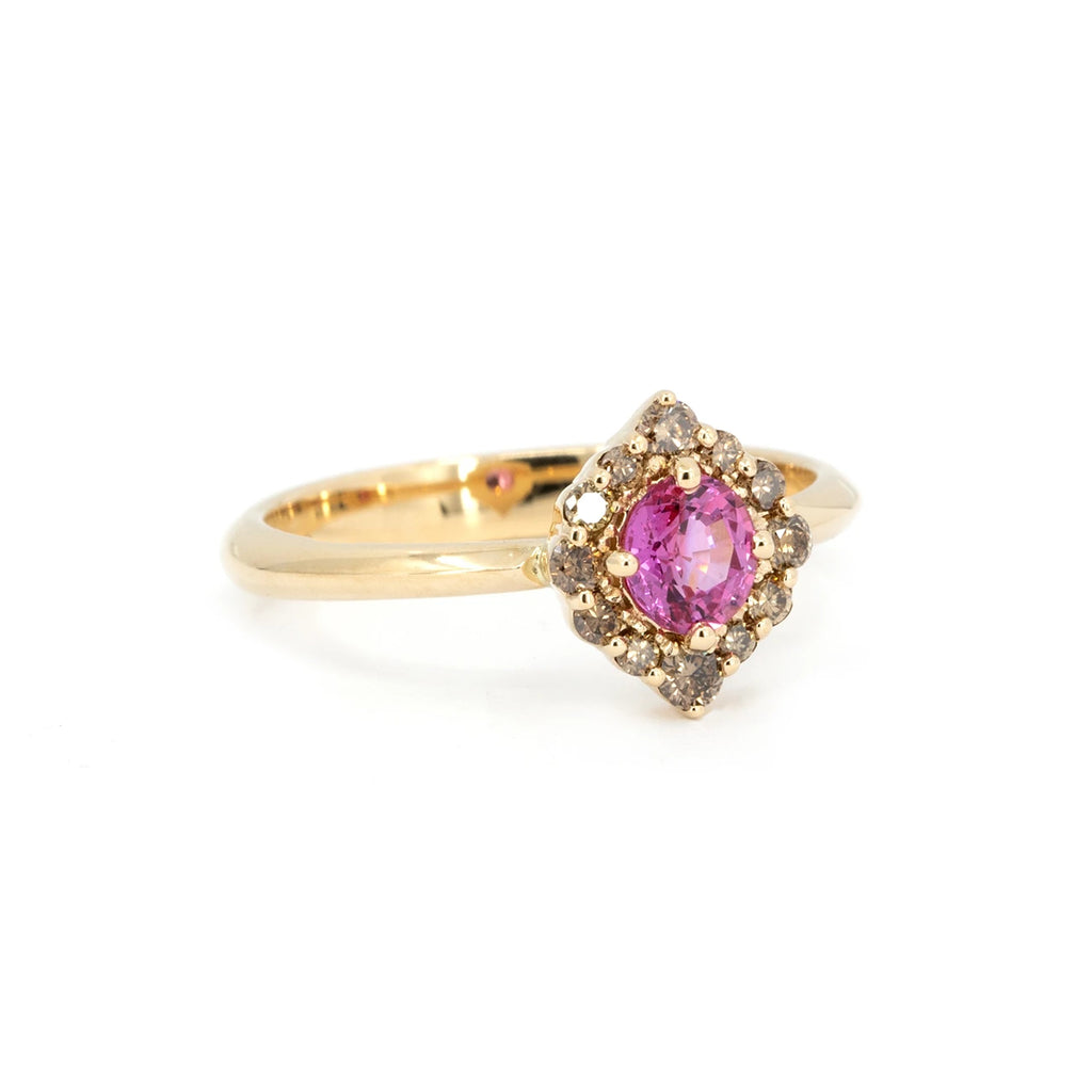Angled view of a yellow gold engagement ring featuring a vivid pink sapphire center stone, surrounded by a pointed halo of natural brown diamonds. Handcrafted by Ruby Mardi in Montreal.








