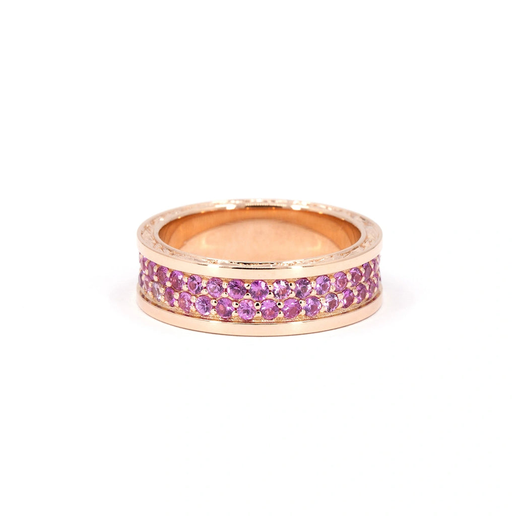 Front view of a bold rose gold band featuring two symmetrical rows of round pink sapphires pavé-set in the center. The sleek design is framed by polished edges and subtle hand engraving. This wide, sculptural ring is designed by Bena Jewelry and handcrafted in Montreal, available exclusively at Ruby Mardi. A contemporary statement wedding band or luxury stacking ring with vibrant color and artisanal detail.