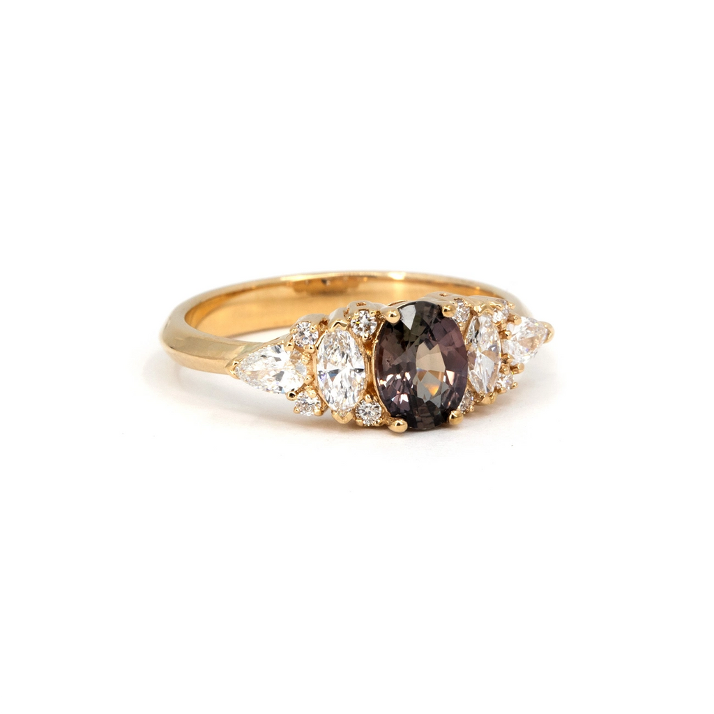 Yellow gold ring featuring an oval plum-colored sapphire at the center, framed by a mix of marquise, pear, and round white diamonds. A one-of-a-kind handcrafted piece by Ruby Mardi in Montreal.