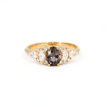 Plum sapphire engagement ring in yellow gold, featuring an oval-cut center stone with shifting hues of purple, bronze, and green, flanked by marquise, pear, and round white diamonds. Handcrafted in Montreal by Bena Jewelry, available at Ruby Mardi.
