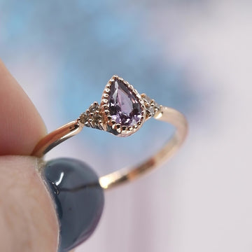 A video shows in close up a pear shape purple sapphire ring set in rose gold with miligrain details. This ring was handmade in Montreal by independent jewellery brand Atelier Emigé.