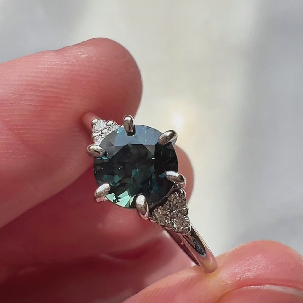 Video of the Talia ring by Maksym Jewelry, featuring a round teal sapphire set in white gold with natural diamond accents. The video captures the ring’s elegant sparkle and refined craftsmanship. Available at Ruby Mardi.